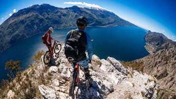 Ein Mountainbiker auf einem felsigen Pfad mit Blick auf einen See und Berge im Hintergrund.
