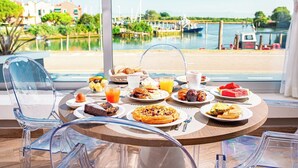 A breakfast table with various dishes and drinks, overlooking a marina with boats and greenery. - Hotel San Giorgio (Caorle)
