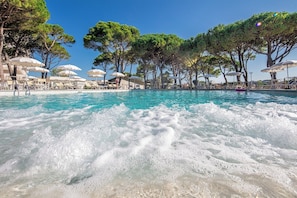 Una piscina con agua cristalina, rodeada de sillones de descanso y sombrillas, con árboles al fondo.