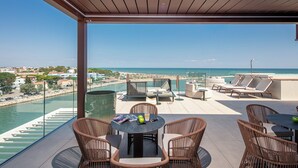 A rooftop terrace with wicker furniture, a round table, and a view of the sea and cityscape. - Hotel San Giorgio (Caorle)