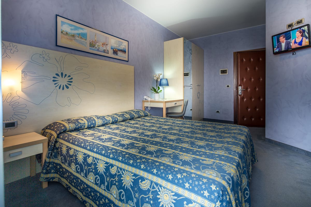 A bedroom with a bed, a desk, a chair, a TV, and a door.