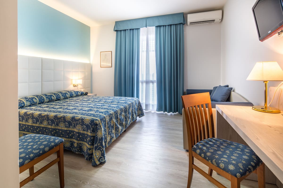A hotel room with a bed, a desk, a chair, and a TV.