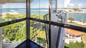 Vista desde un edificio alto con ventana de vidrio, con vista a una zona costera con vegetación y una playa.