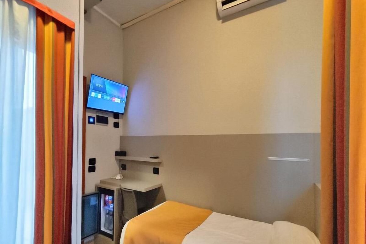 Una habitación de hotel con cama, escritorio, televisor y una pequeña kitchenette.