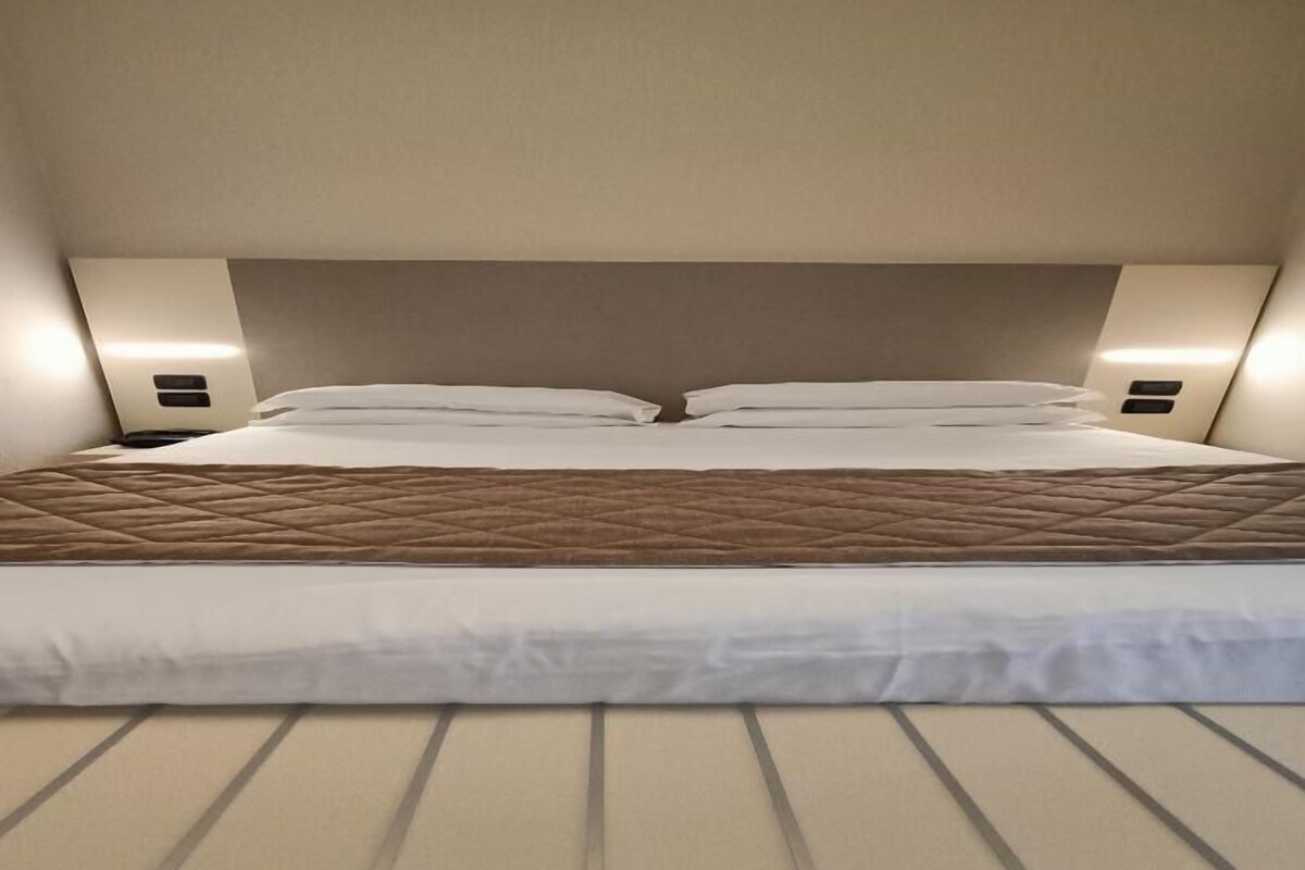 Una cama con cabecera acolchada, dos mesitas de noche y un suelo de tono claro.