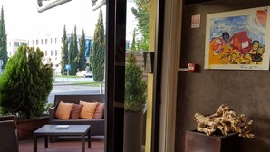Una entrada con puerta de vidrio que conduce a un espacio al aire libre con mobiliario de mimbre y una planta en maceta.