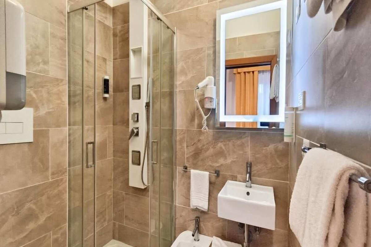 Un baño moderno con ducha de mampara de vidrio, lavamanos, espejo y secador de pelo.