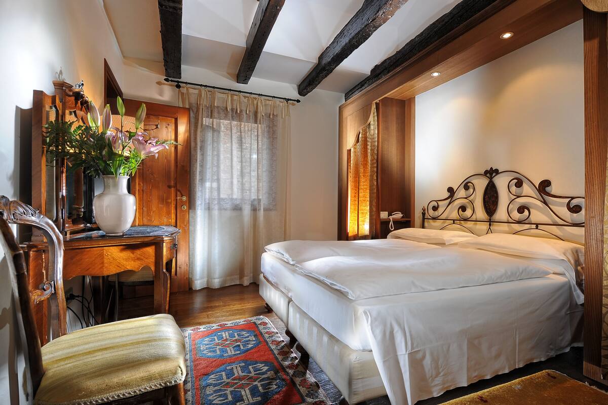 Une chambre à coucher avec un lit en bois, un bureau agrémenté d’un vase de fleurs, une chaise et un tapis à motifs.