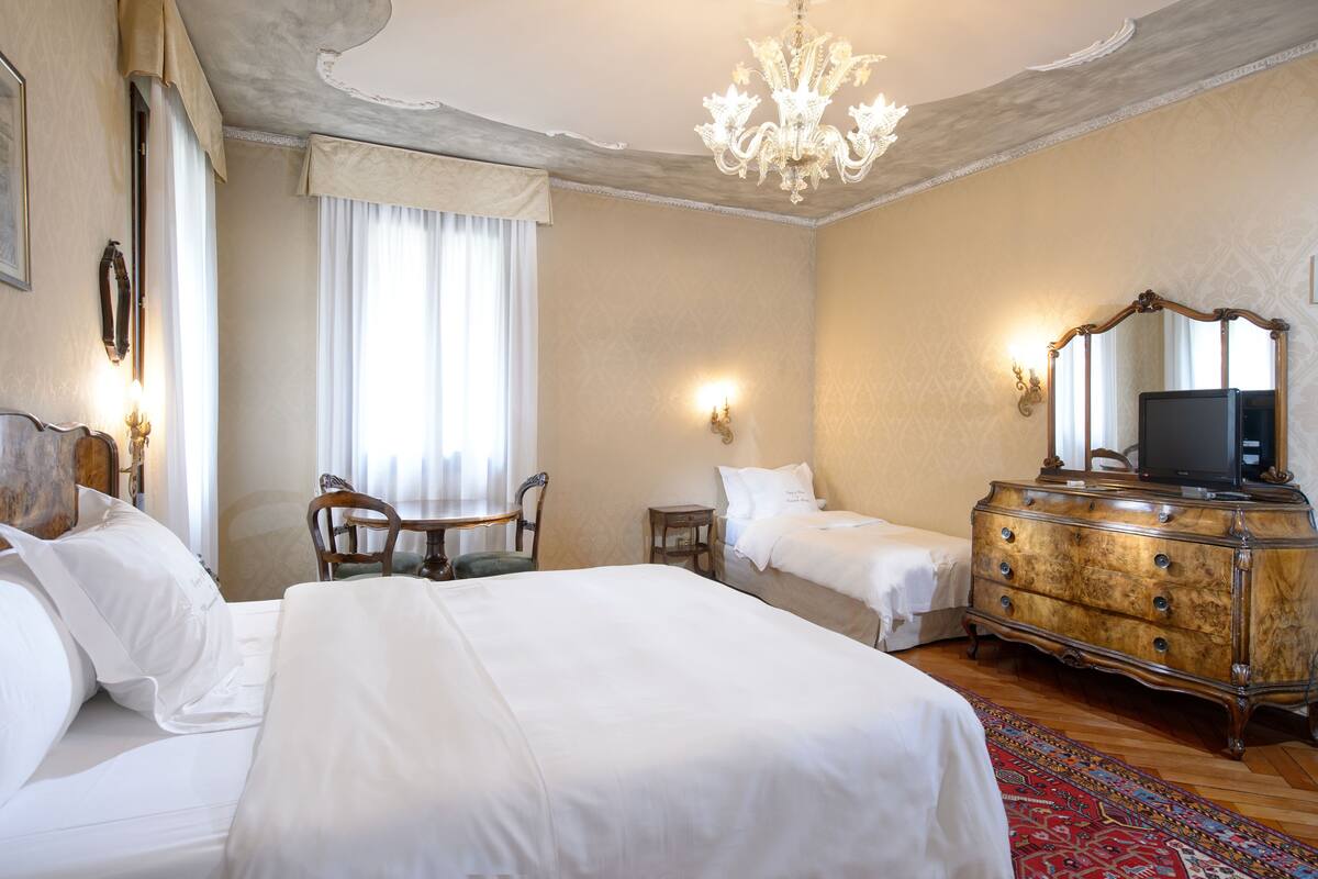 Une chambre d’hôtel avec deux lits, une commode en bois, un bureau et un lustre.