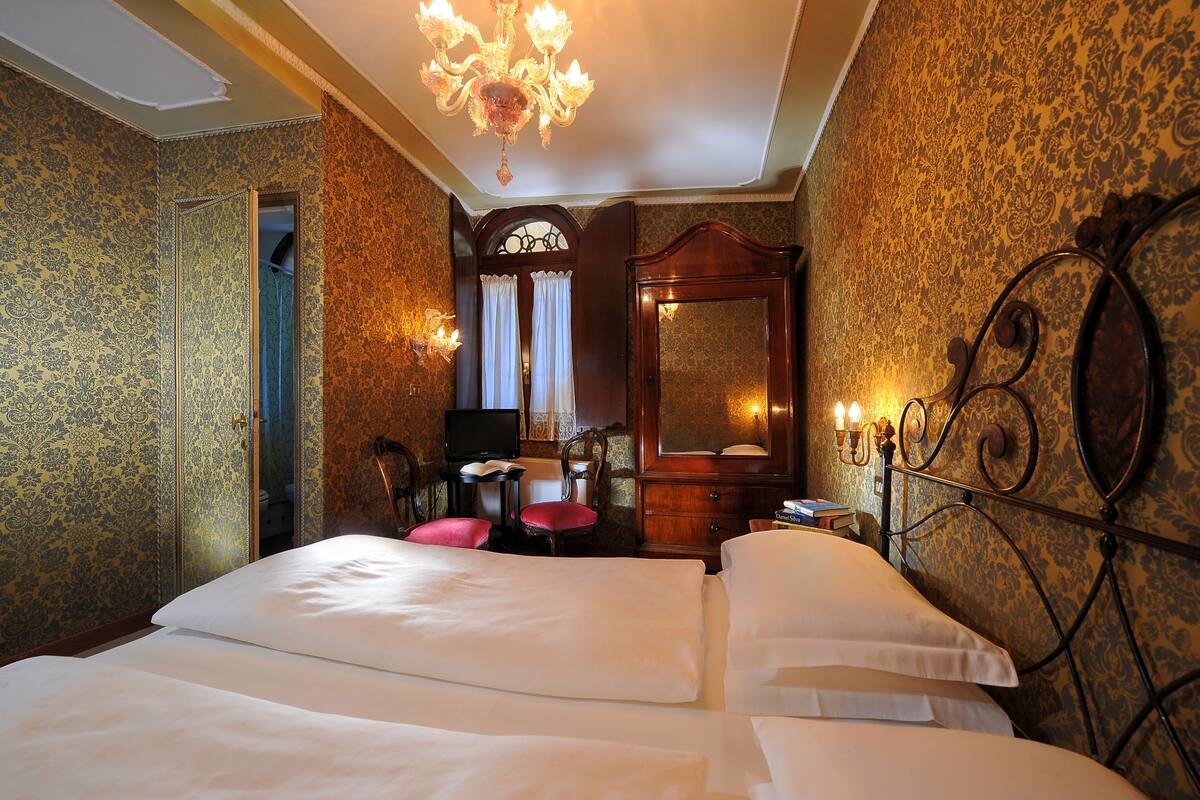 Une chambre d’hôtel avec un lit double, un bureau avec une chaise, un miroir et un lustre.
