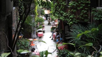 A narrow alley with tables and chairs, surrounded by lush greenery and brick walls.