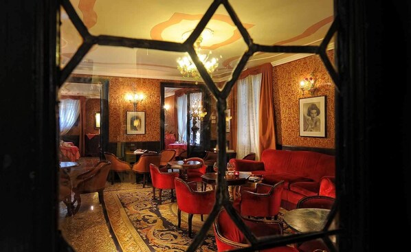 A room with a patterned carpet, red upholstered chairs, a red sofa, and a chandelier.
