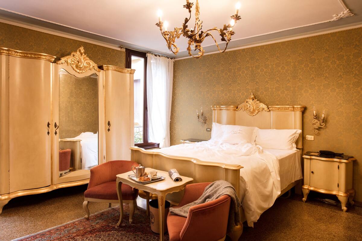 Une chambre d’hôtel comprenant un lit, un bureau avec une chaise, une armoire et un lustre.