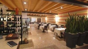 A restaurant with wooden ceiling beams, tables with white tablecloths, and potted plants. - Hotel Villa Altura (Ospedaletto Euganeo)