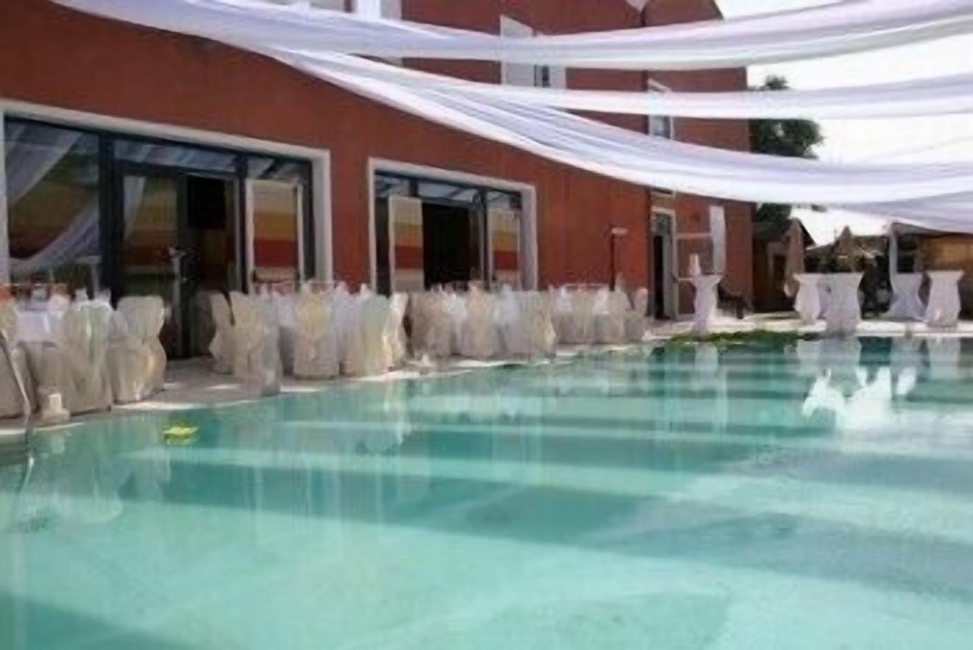 A swimming pool with white drapes and covered chairs, suggesting a private or semi-private setting.
