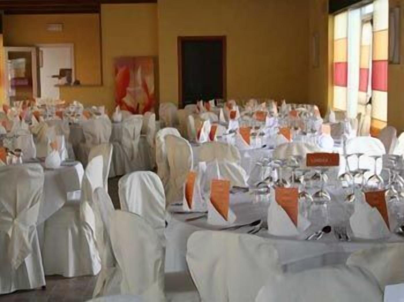 A banquet hall with round tables set for dining, white tablecloths, and orange sashes.