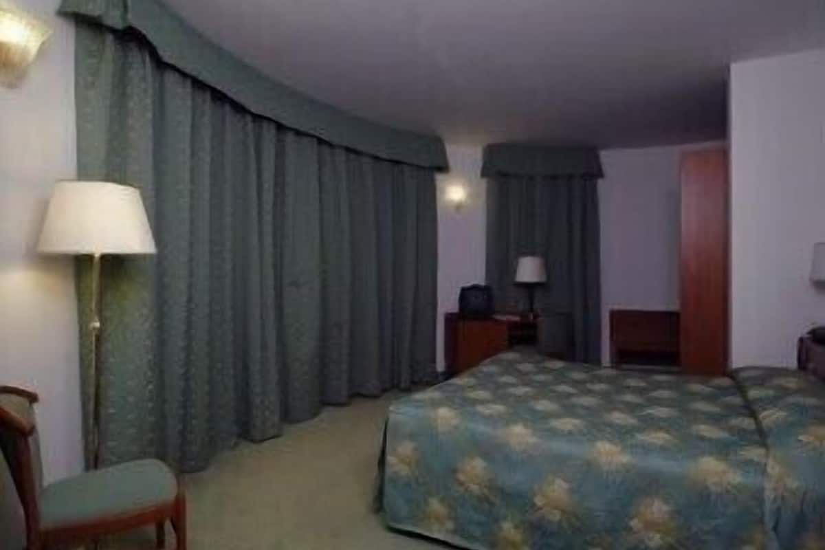 A hotel room with a bed, a chair, a desk with a lamp, and curtains.