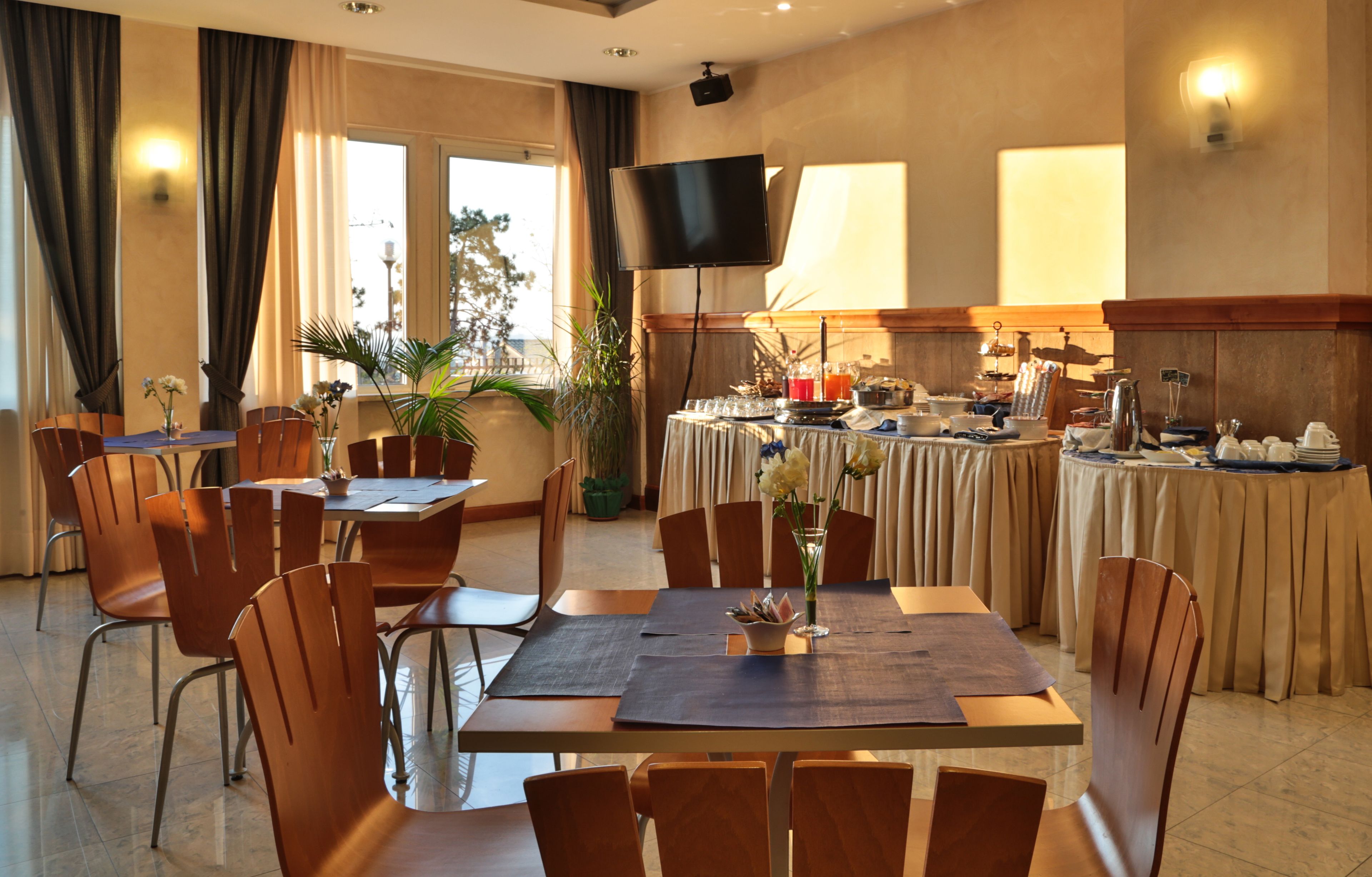 Un espace de restauration d'hôtel comprenant une grande table, des chaises, un téléviseur et un buffet.