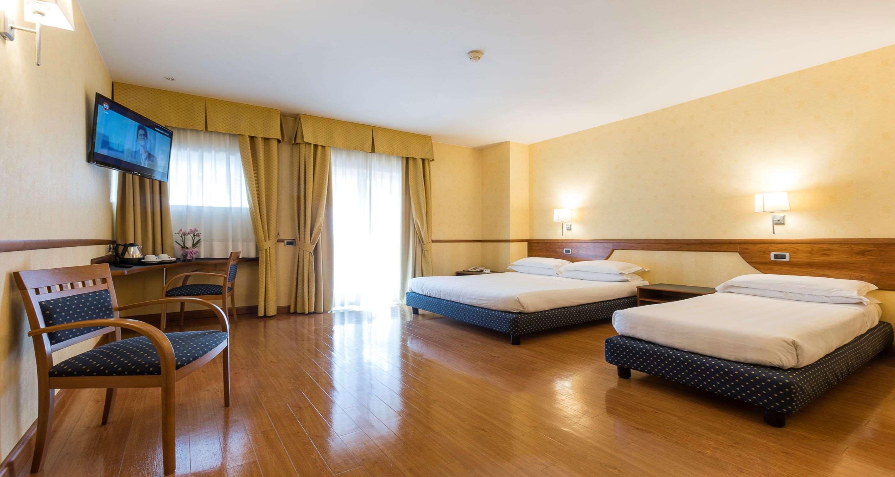 A hotel room with two beds, a desk, a chair, and a TV.