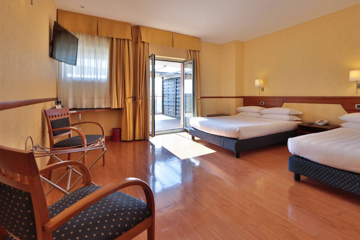 Una camera d'albergo con due letti, televisore, una sedia e una finestra con tende.