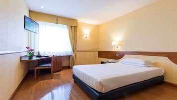 Une chambre d’hôtel équipée d’un lit, d’un bureau, d’une chaise et d’un téléviseur fixé au mur.