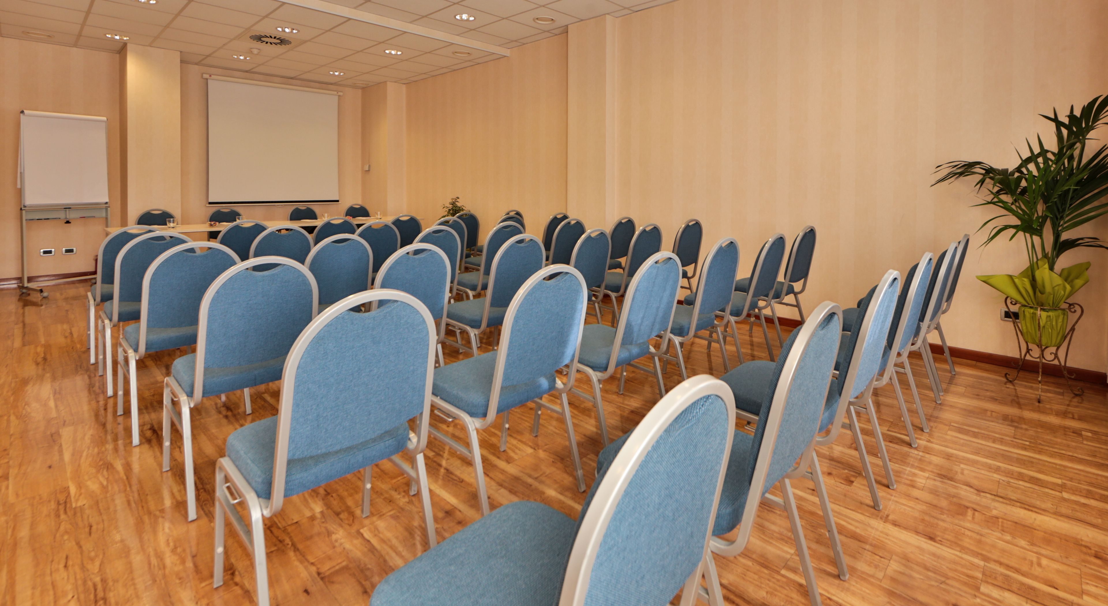 A conference room with rows of blue chairs, a whiteboard, and a projector screen.