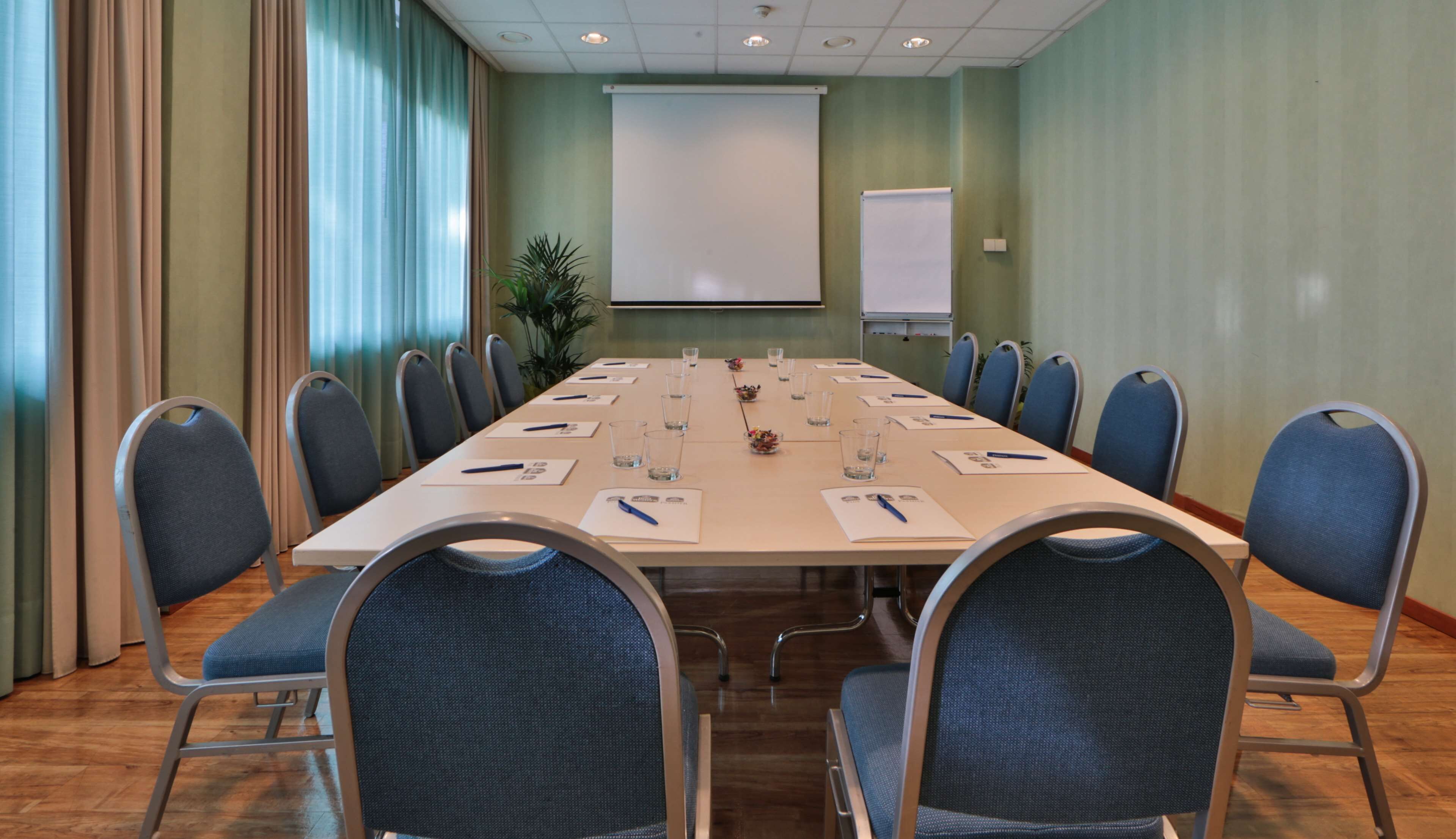 A conference room with a long table, chairs, and a projector screen.