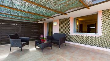 An outdoor patio area with wicker furniture, a glass table with a vase, and a patterned wall.