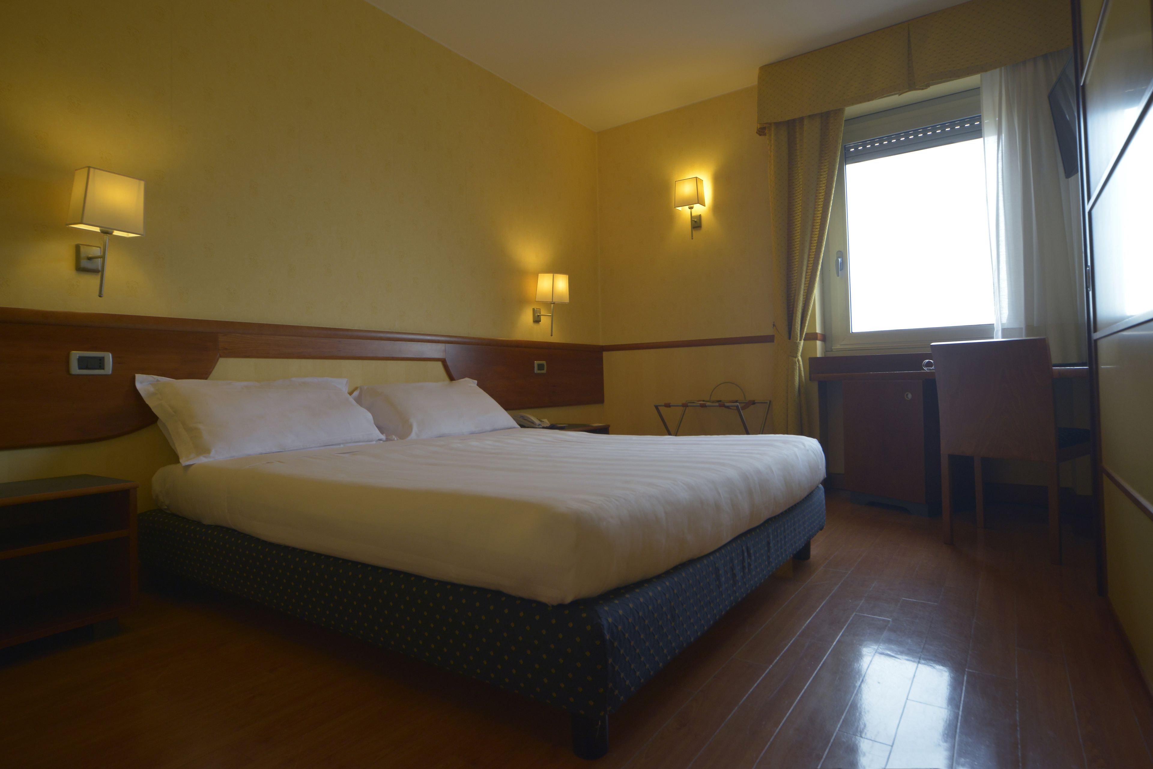 A hotel room with a large bed, two bedside tables, a desk, and a chair.