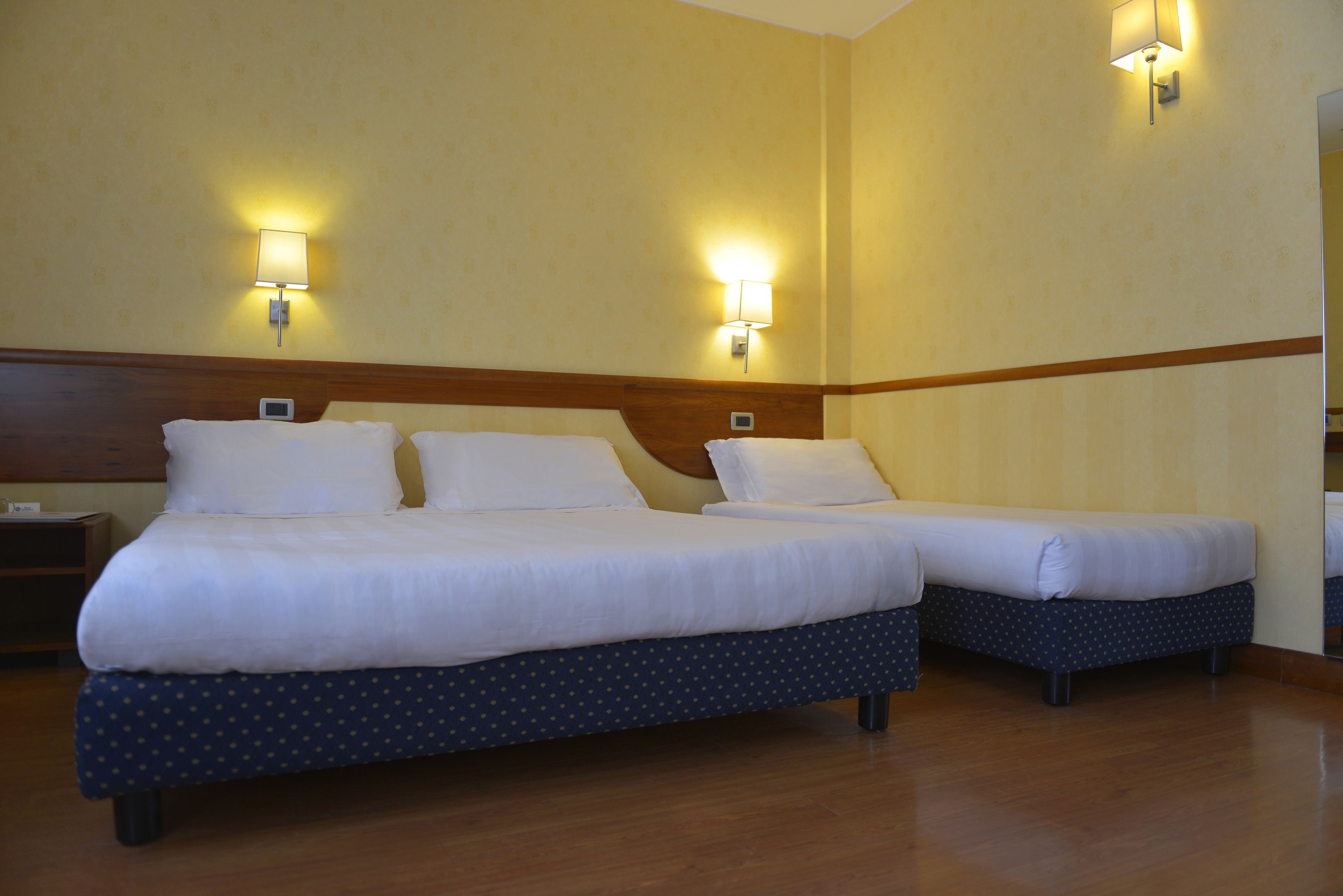 A hotel room with two beds, wooden headboards, and wall-mounted lamps.