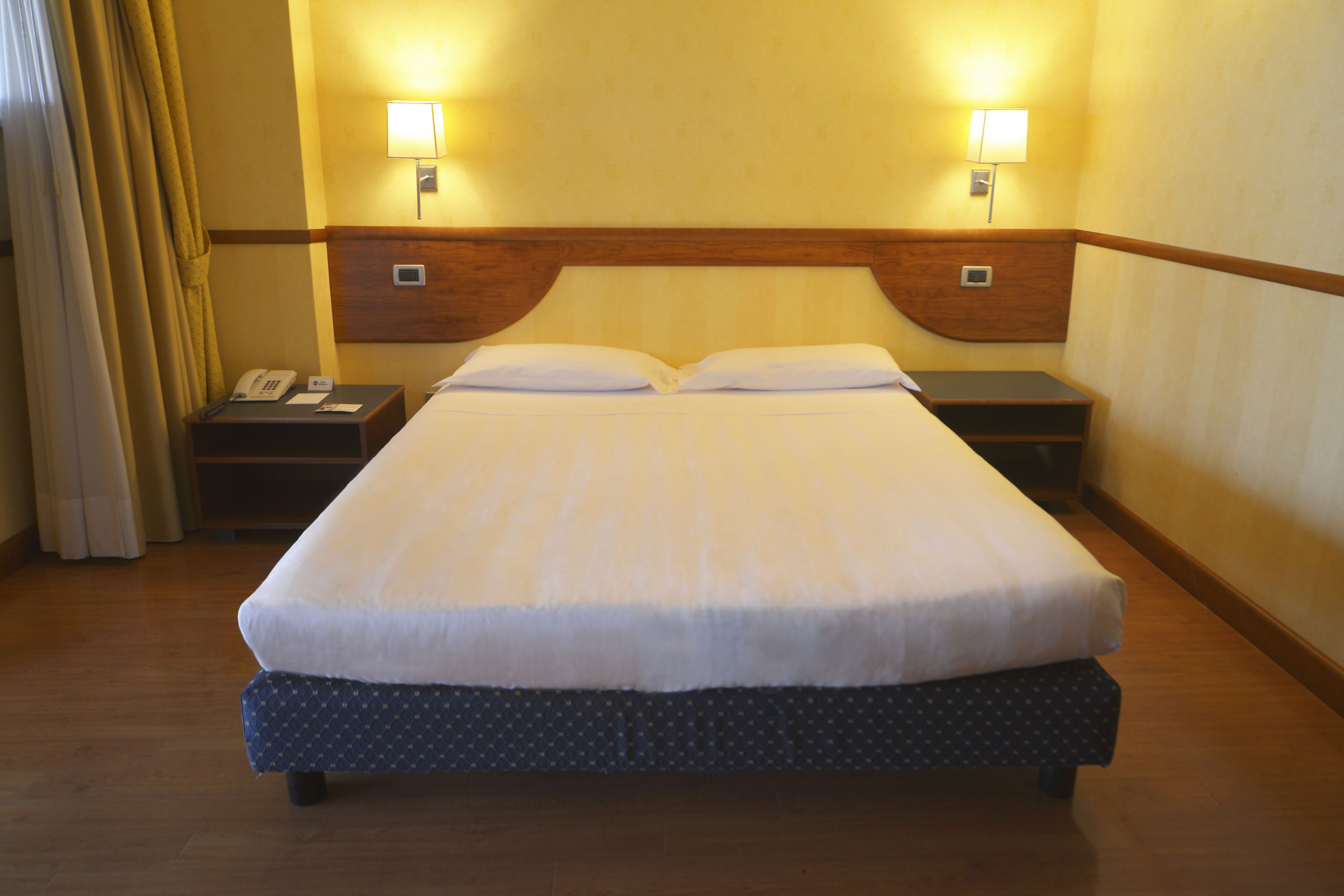 Una camera d'albergo con un letto grande, due abat-jour, un telefono e un comodino.