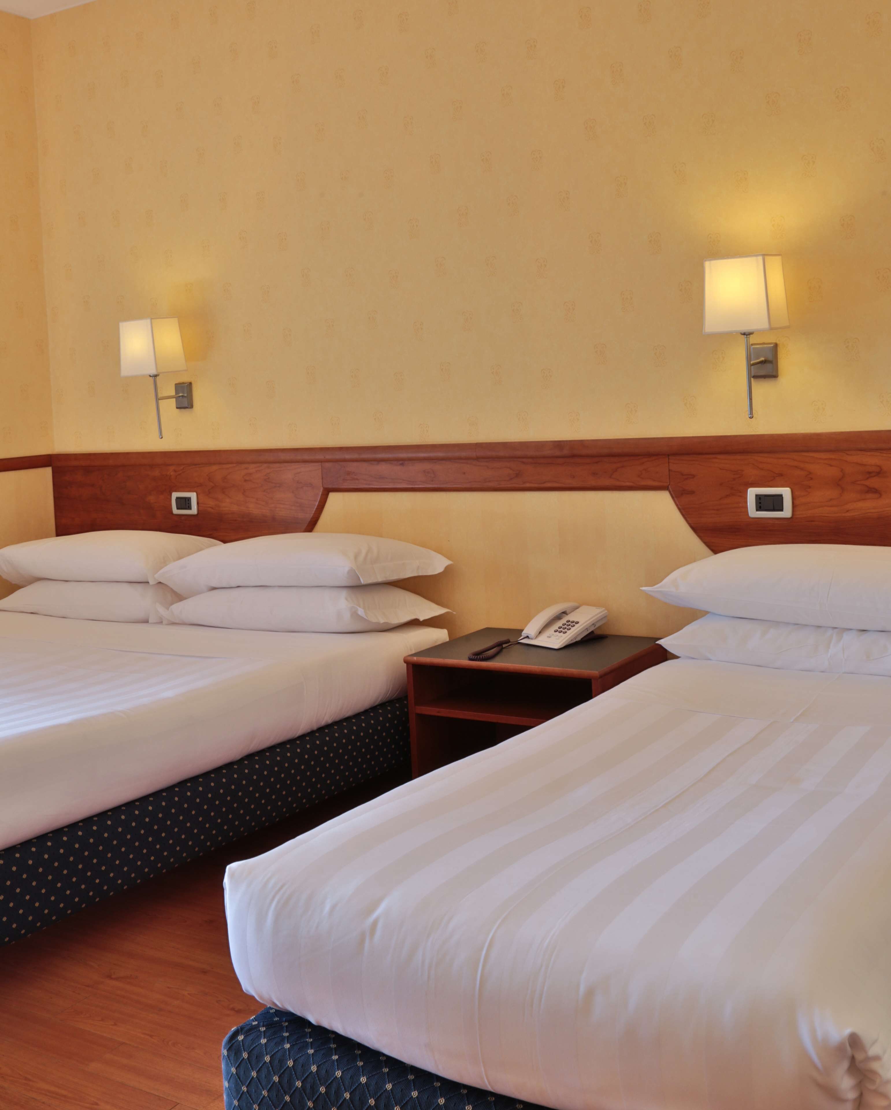 Habitación de hotel con dos camas, una mesita de noche con teléfono y lámparas de pared.