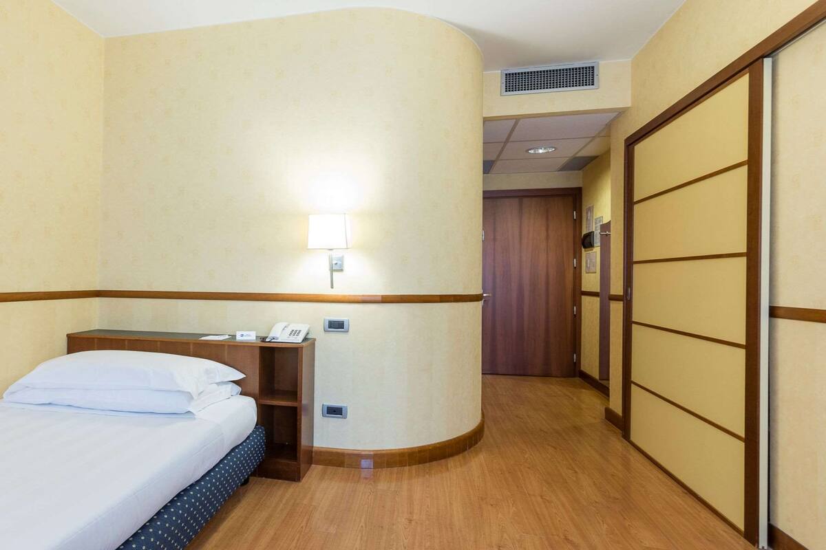Una camera d'albergo con un letto, un comodino, una lampada e un armadio.