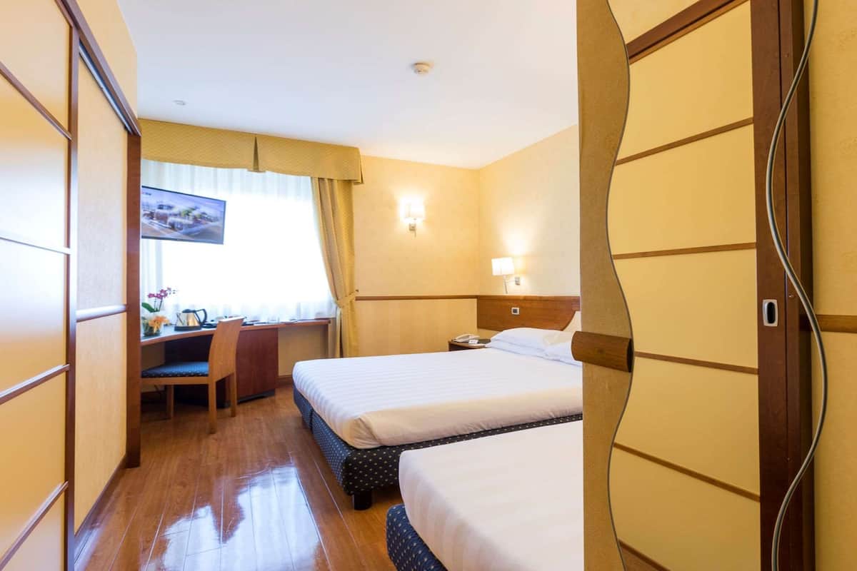 Camera d'albergo con due letti, una scrivania, una sedia e un televisore.