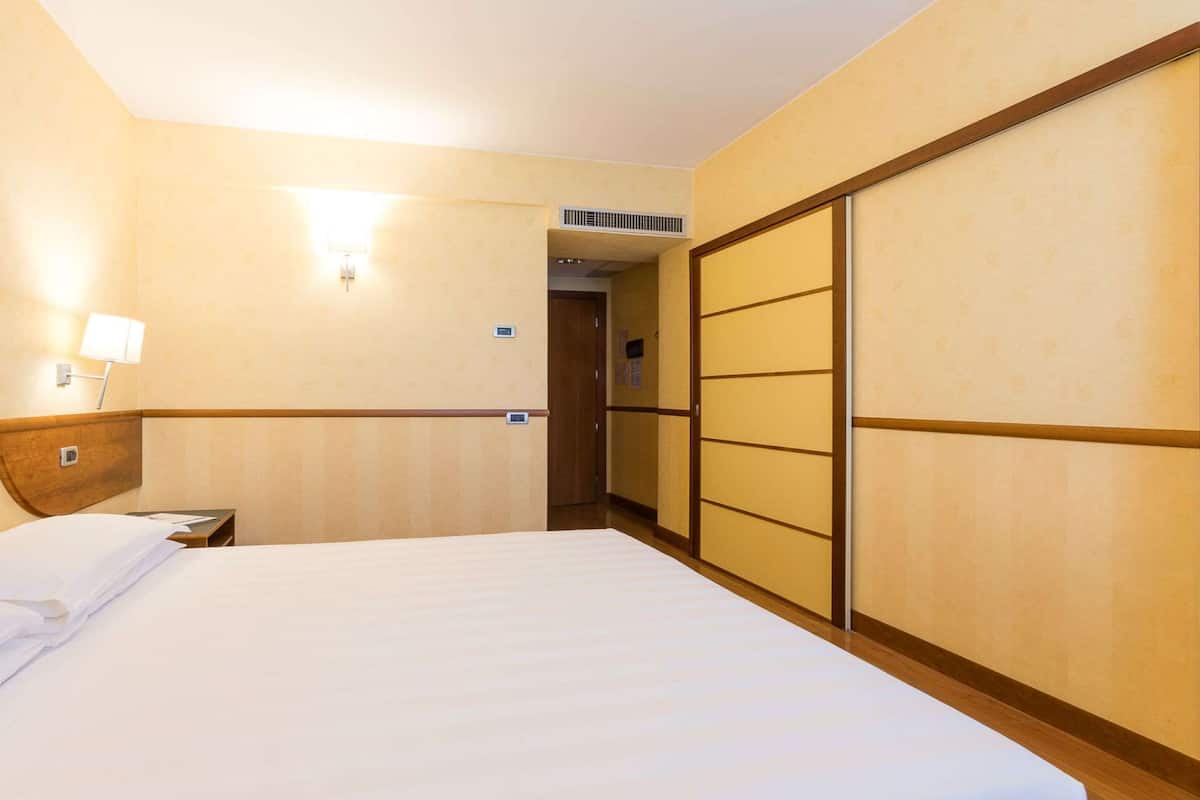 Camera d'albergo con un letto, un comodino, una lampada e porte scorrevoli.