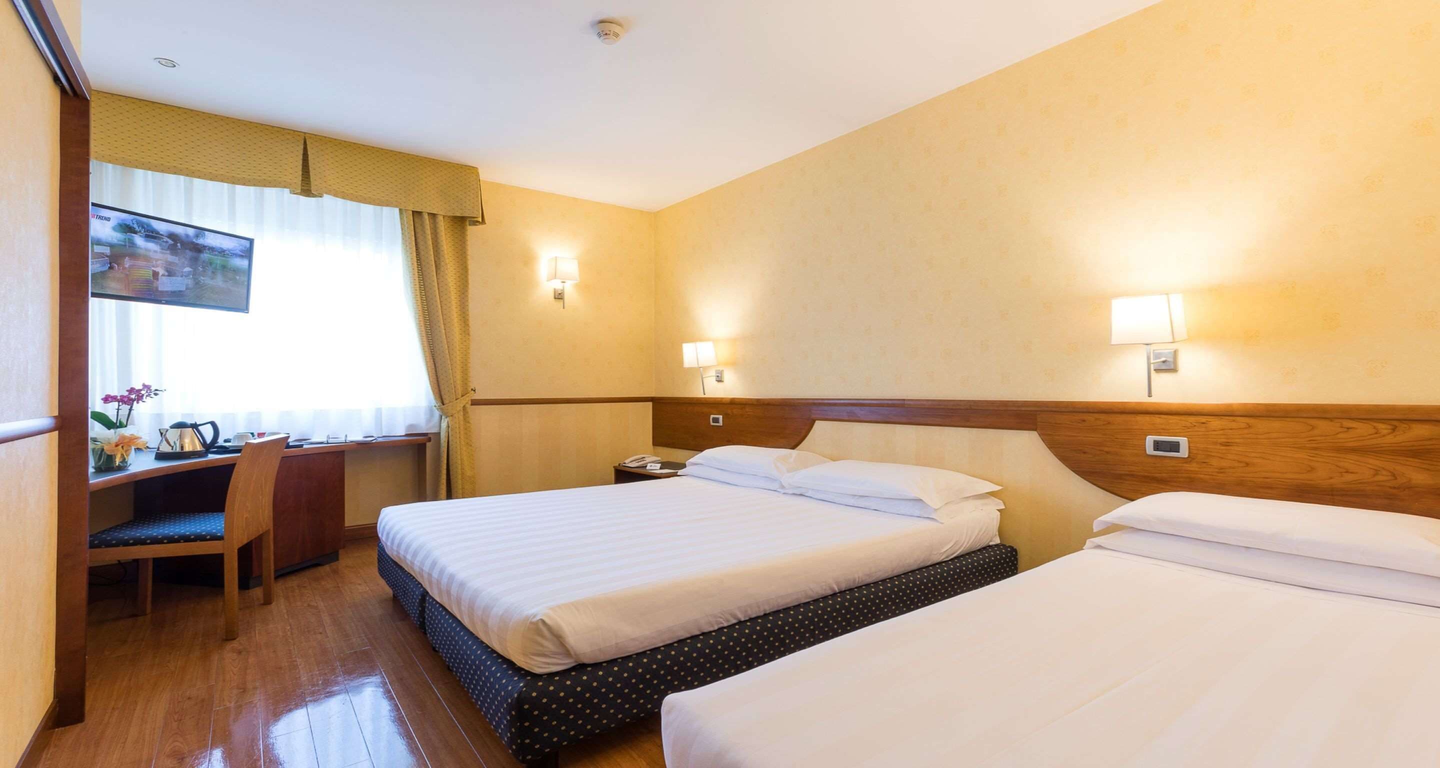 A hotel room with two beds, a desk, and a TV.