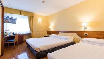 A hotel room with two beds, a desk, and a TV.
