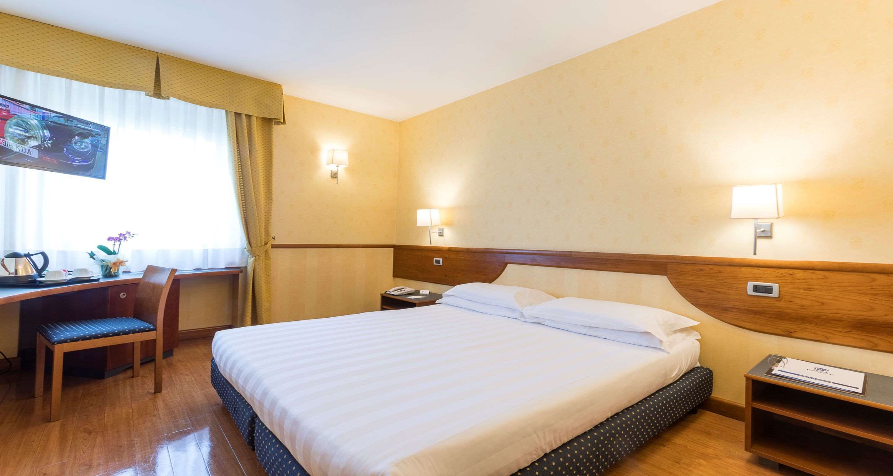 Een hotelkamer met een groot bed, een bureau met stoel, een televisie en twee bedlampen.