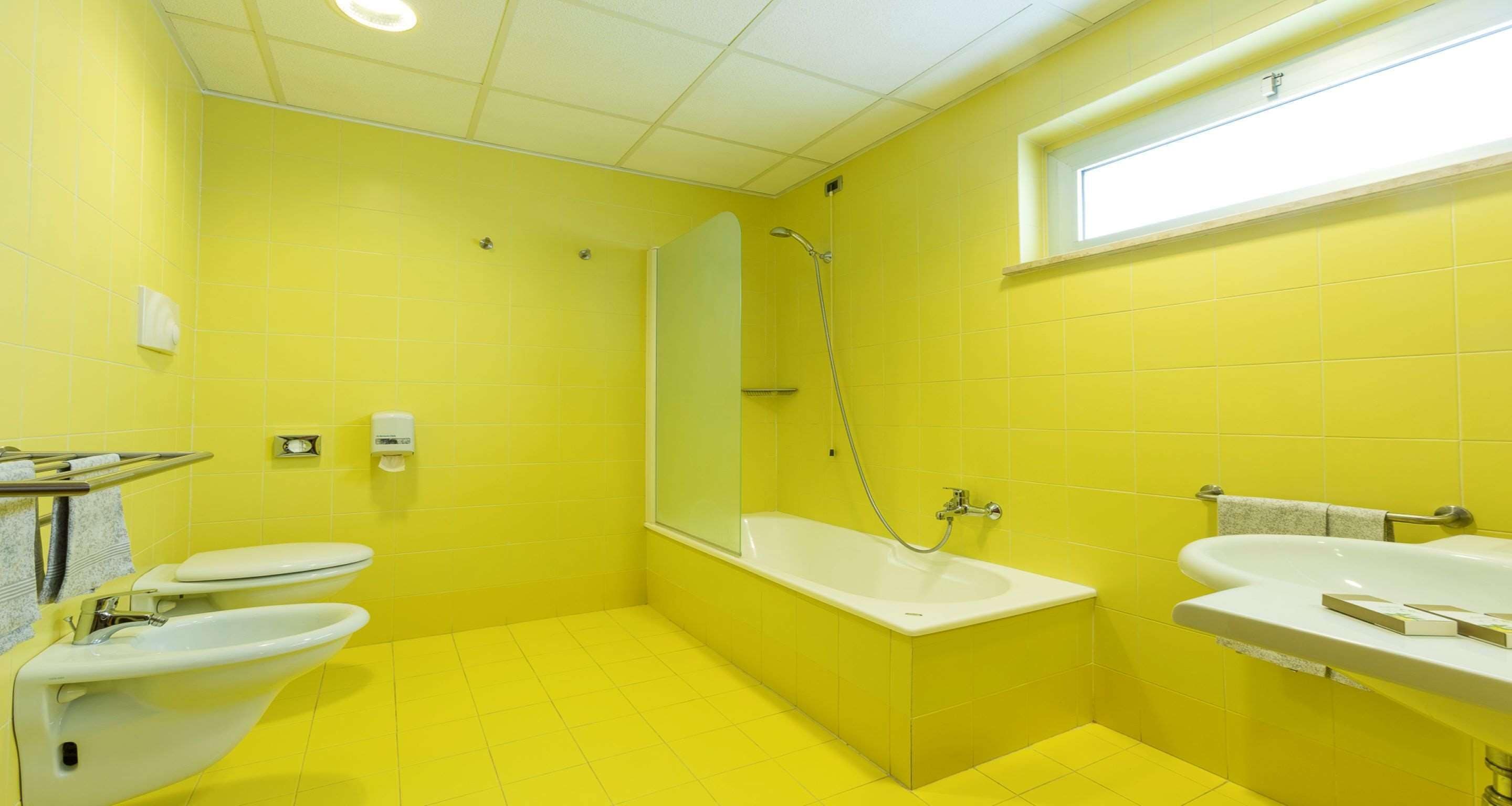Un bany amb rajoles grogues, una banyera, un lavabo i un vàter.