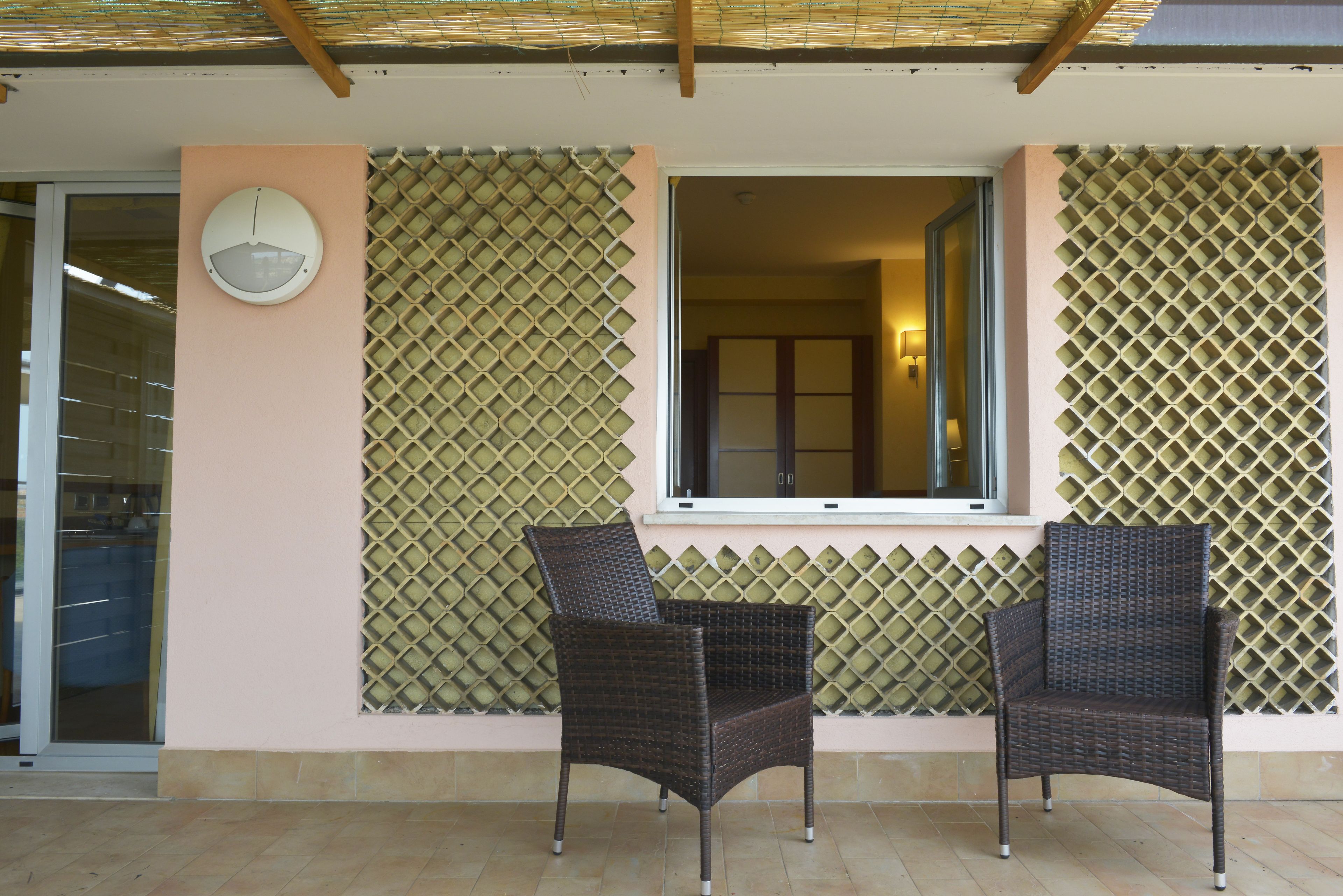 Una habitación con dos sillones de mimbre, un ventanal y un reloj en la pared.