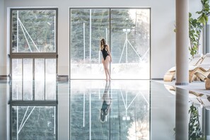 Un espacio interior amplio con un gran ventanal, una persona de pie y un reflejo en el suelo.