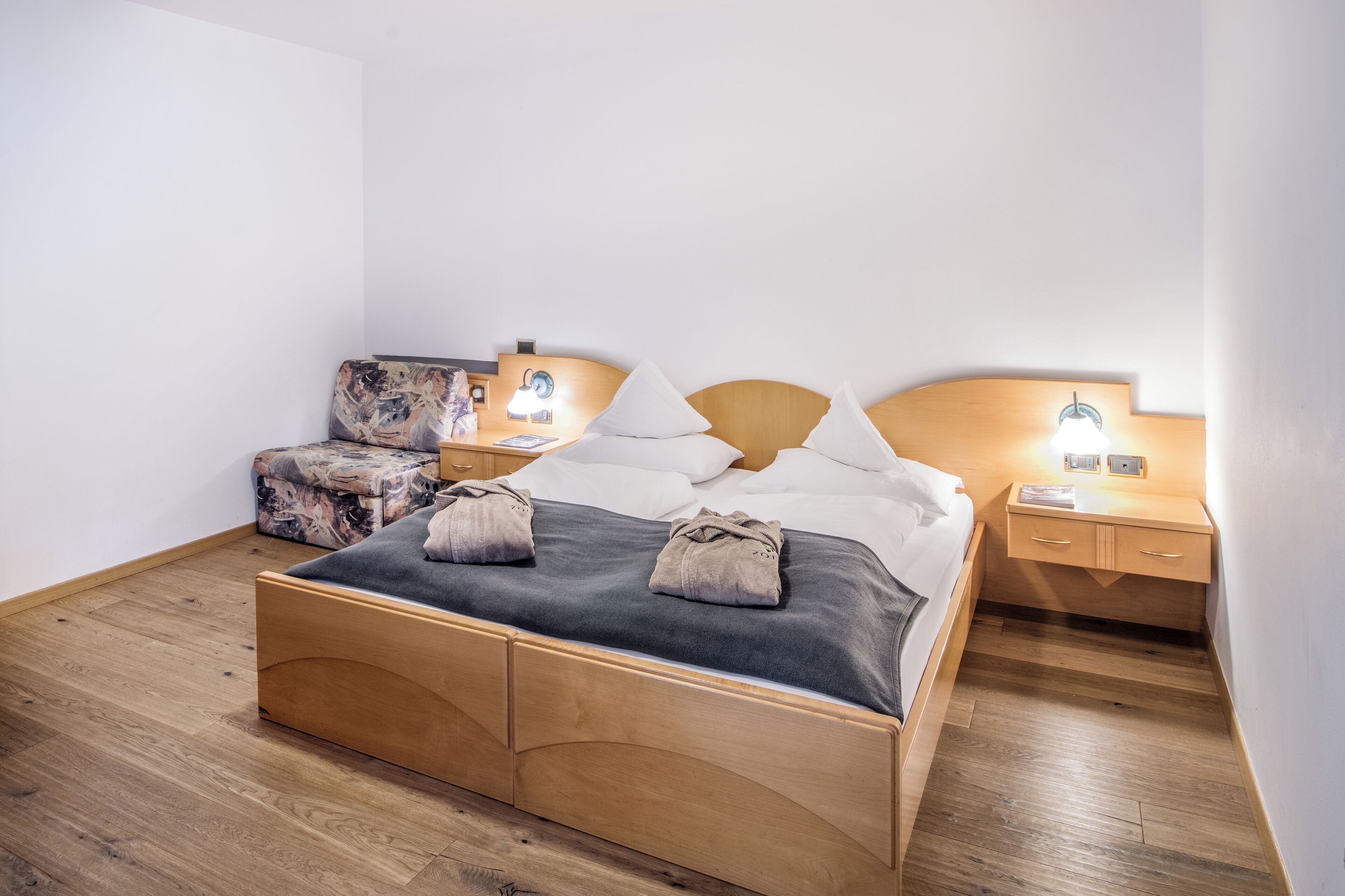 A neatly arranged bedroom with a wooden bed, a small sofa, two bedside tables with lamps, and a nightstand.