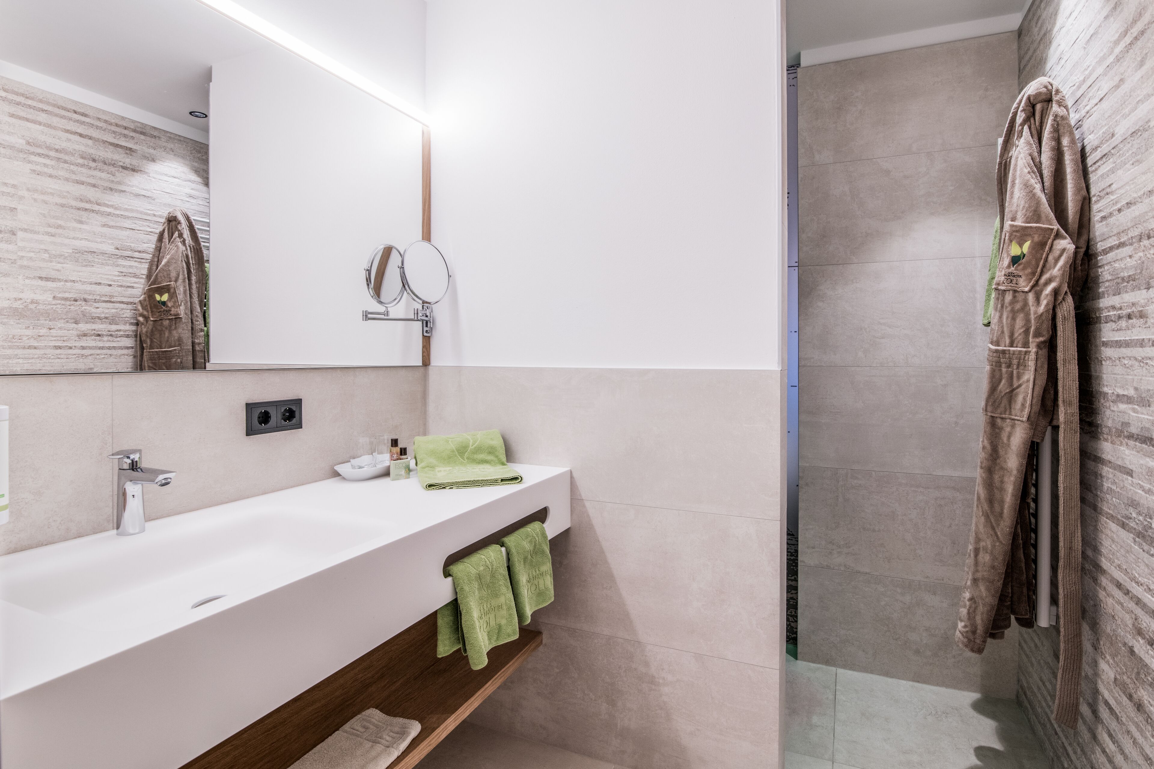 A modern bathroom with a white sink, mirror, and green towels.