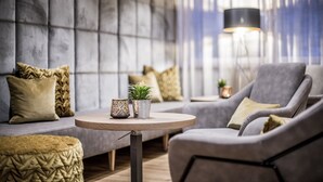 A modern living room with a grey sofa, a round wooden coffee table, and a grey armchair. There is a floor lamp and a small potted plant on the table. - Sporthotel Zoll (Vipiteno)