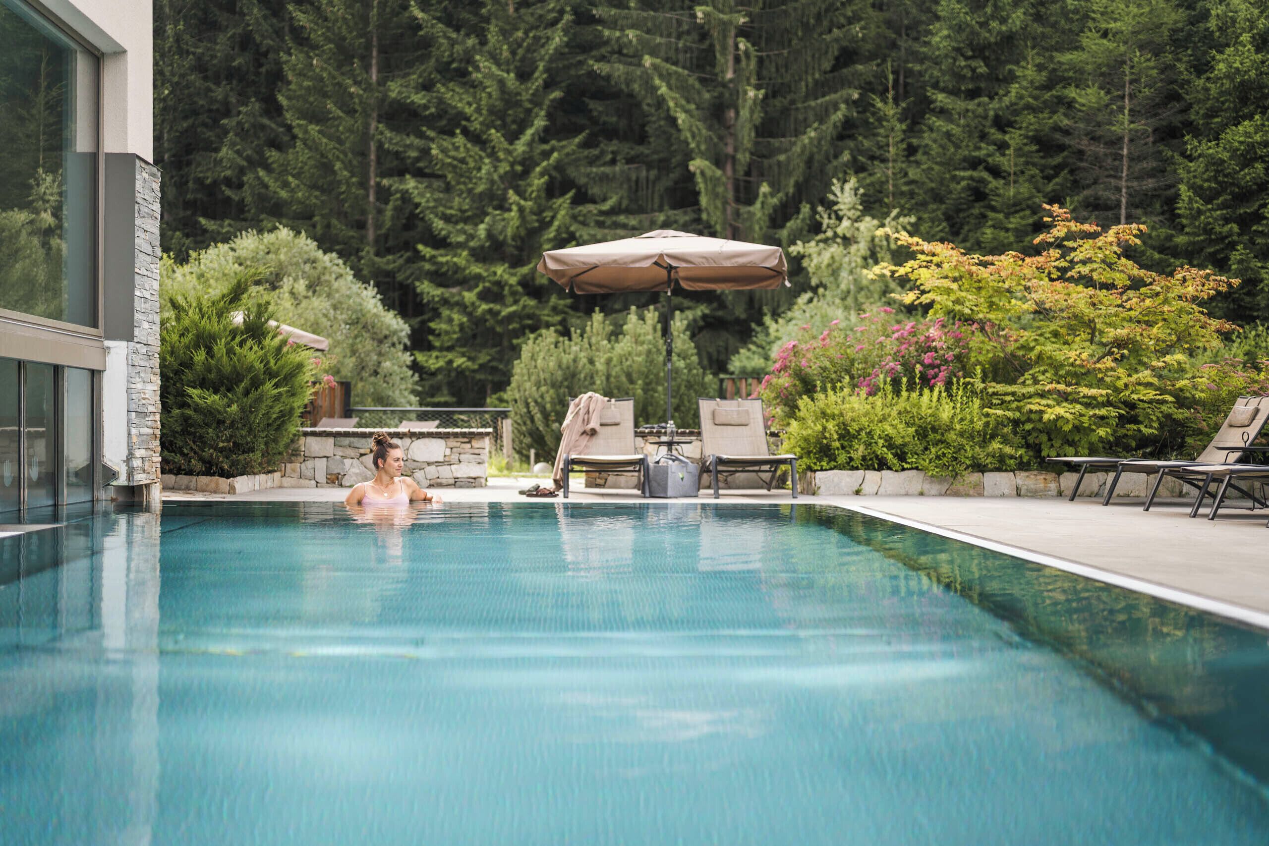 A swimming pool with a person in the water, surrounded by greenery and outdoor furniture.