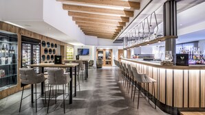 A modern bar area with wooden ceiling beams, a bar counter, and seating. - Sporthotel Zoll (Vipiteno)