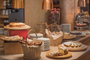 A bakery display with various pastries and bread, including a cake on a stand and baskets of bread. - Bellavista Relax Hotel (Levico Terme)