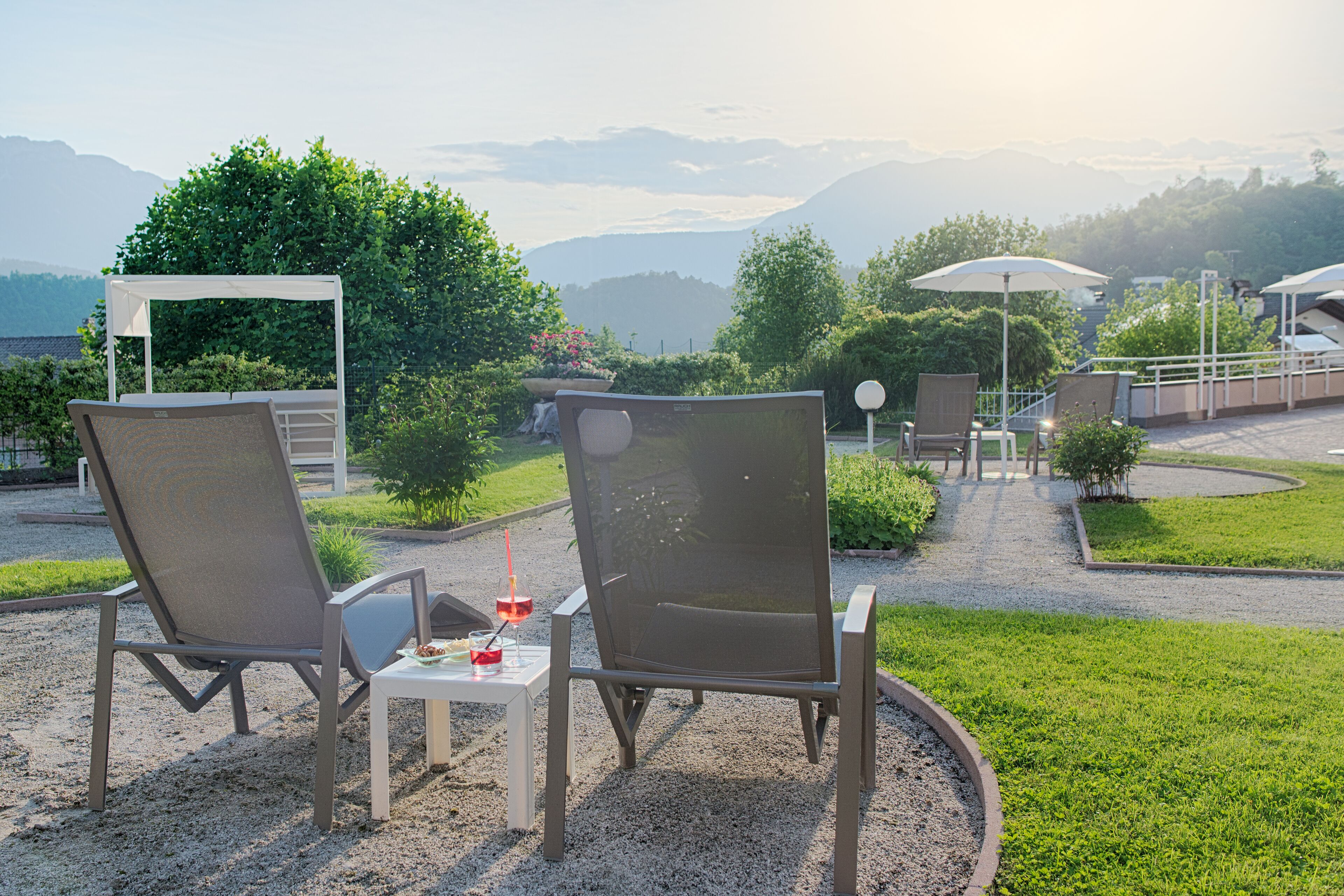 Two outdoor seating areas with chairs and tables, surrounded by greenery and a view of distant mountains.