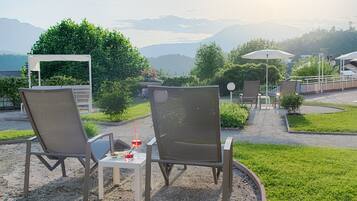 Two outdoor seating areas with chairs and tables, surrounded by greenery and a view of distant mountains.