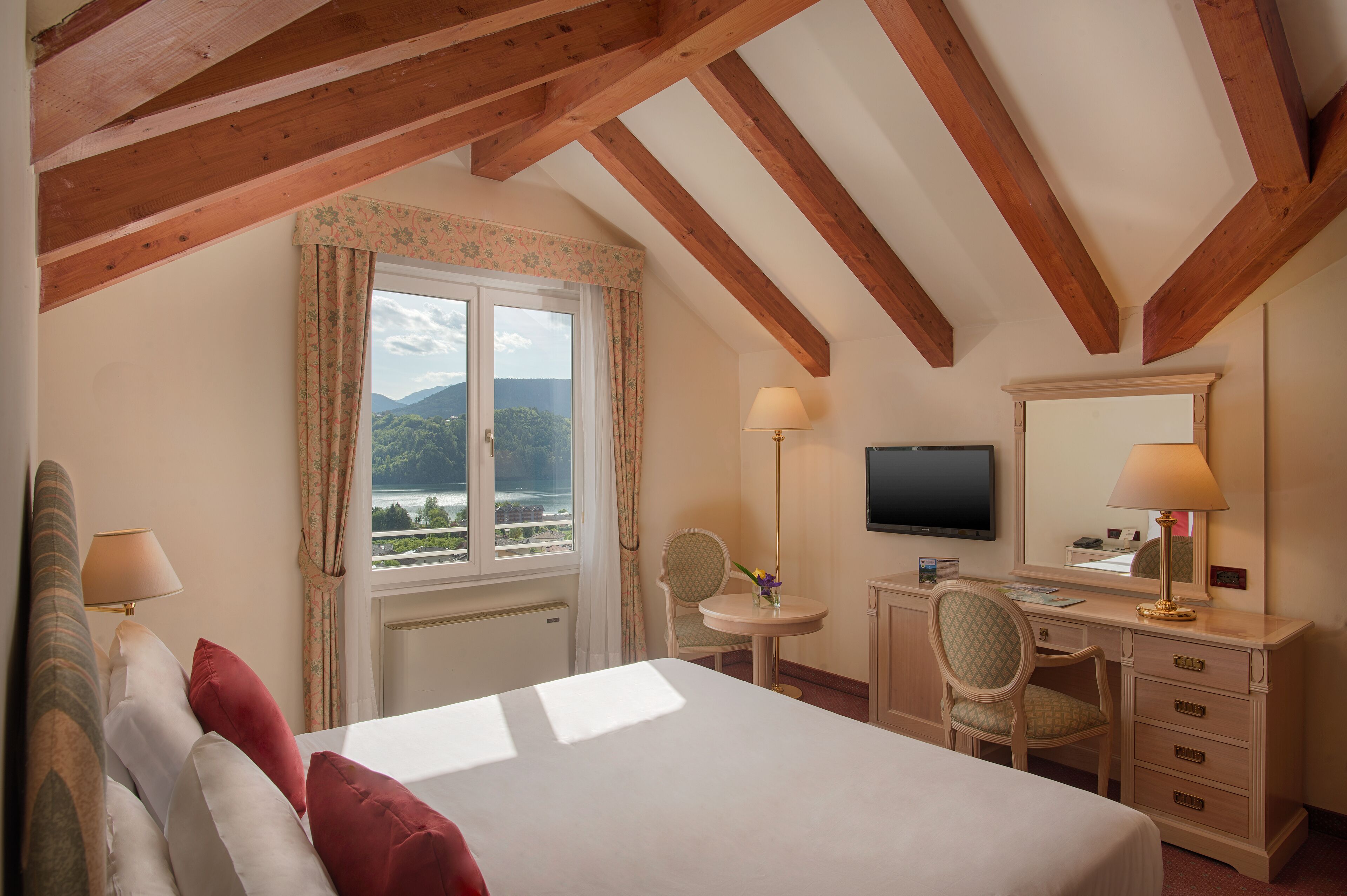 Habitación de hotel con cama, escritorio, silla, televisor y ventana con vistas a montañas.